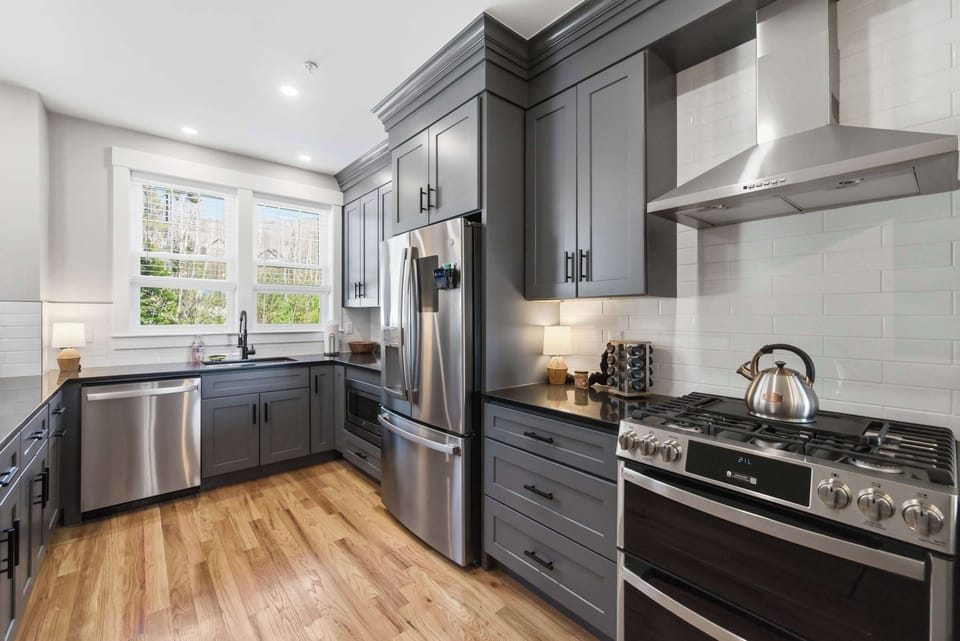The chef's kitchen is fully equipped for the group — gas range, stainless hood, French-door fridge, and custom two-tone shaker cabinets throughout.