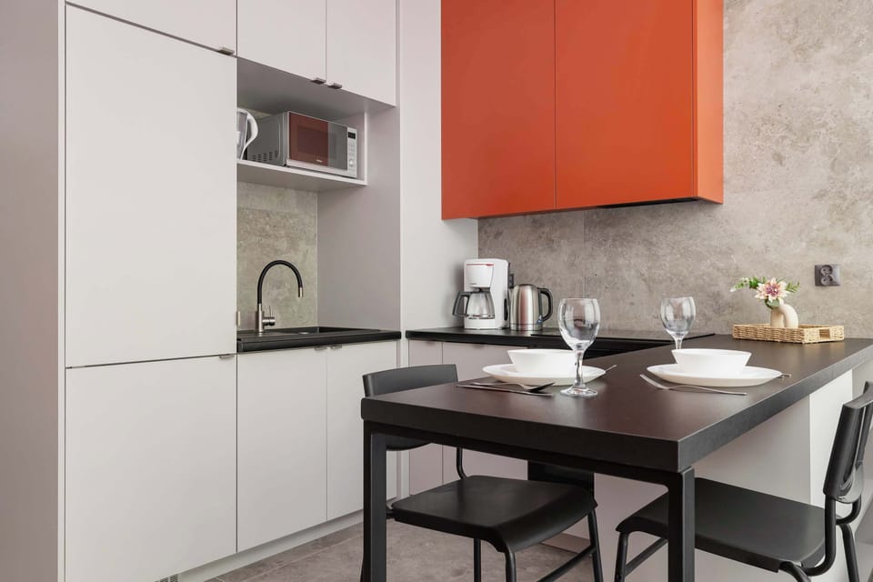 Compact open-plan kitchenette with modern appliances, dining table and stylish orange accents.