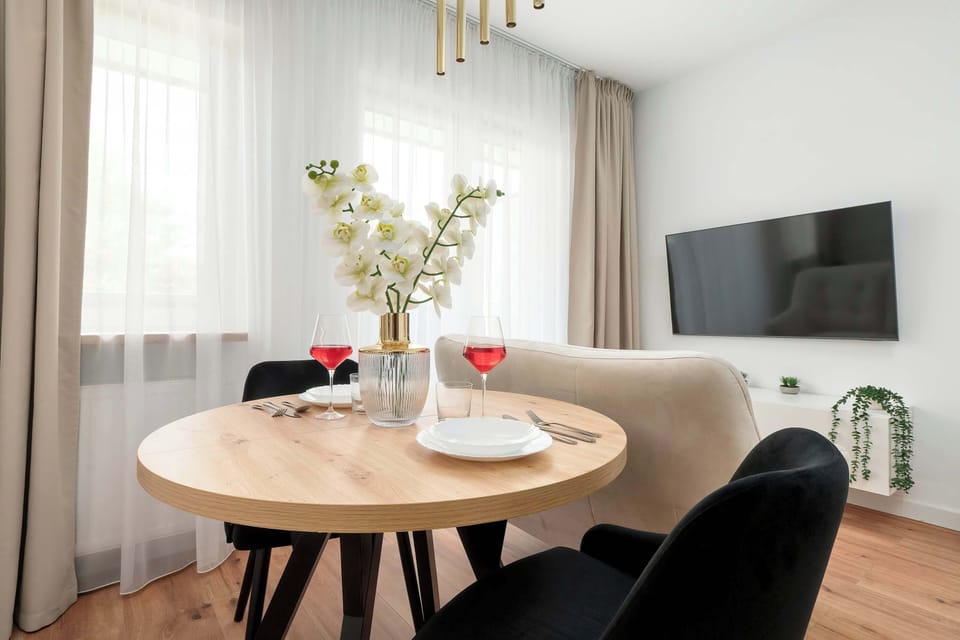 A dining setup with a round table, dark chairs, and a vase of flowers placed near a television.