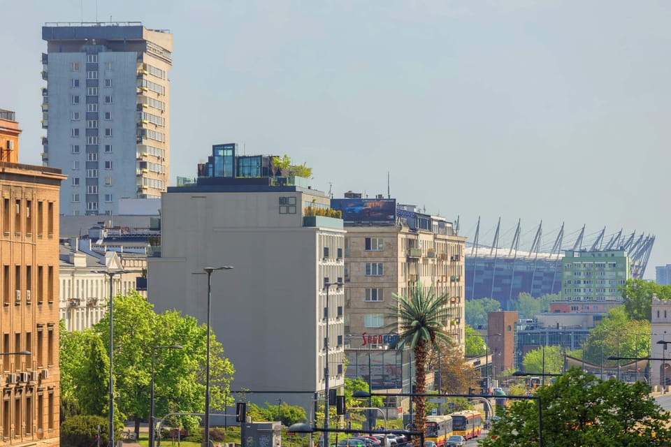 An elevated urban view overlooking rooftops, greenery, and modern buildings in the distance.