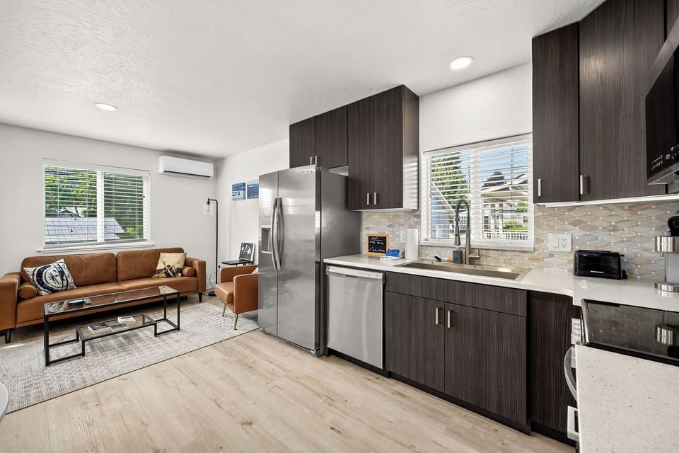 Open-concept living space where modern design meets comfort. Sunlight floods through windows, highlighting the stylish kitchen with gleaming countertops and stainless steel appliances, perfect for unwinding.