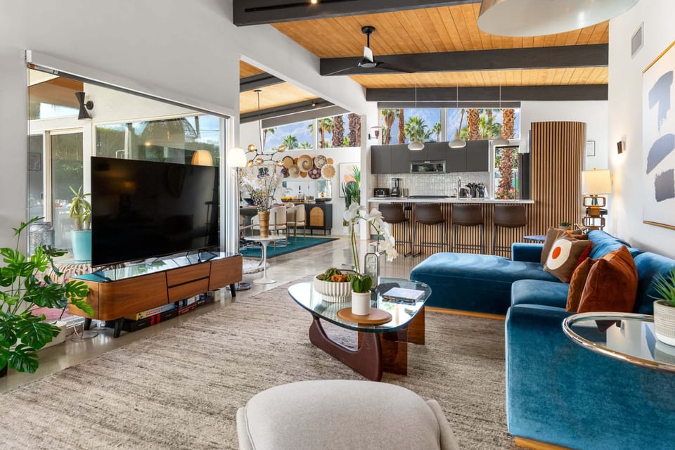 Relax in this stunning mid-century modern living space where rich blue velvet seating meets warm wood tones and desert views beyond.