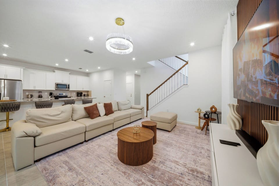 Welcome to a bright living area with a spacious sectional sofa and earthy throw pillows, perfect for lounging. The warm wooden coffee table and soft rug create a cozy vibe, while modern lighting enhances the inviting atmosphere.