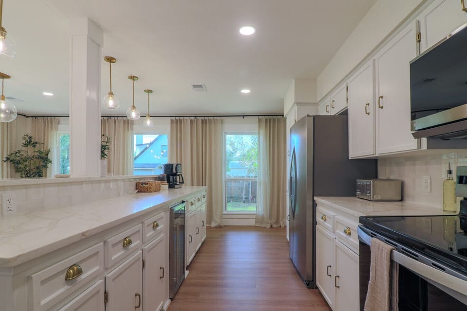 Remodeled kitchen with new electric range, stainless fridge, wine cooler, dual coffee maker, toaster, and ample cabinet storage. Gold hardware finishes and natural light from a large window. Everything a family needs to cook comfortably.