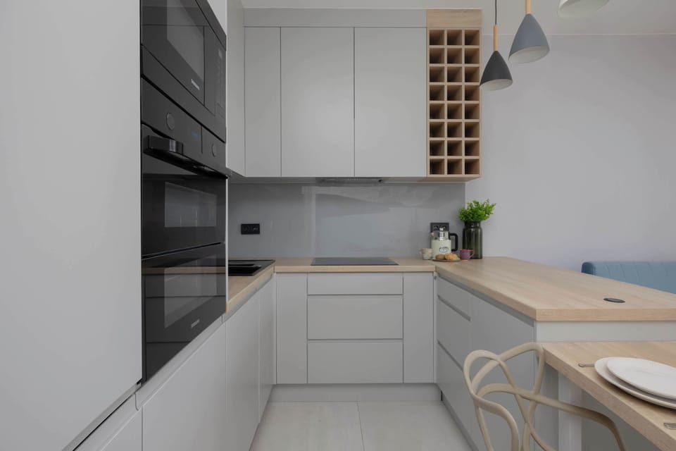 A sleek kitchenette with white cabinets, modern appliances, and wooden accents. The clean design gives the space a contemporary and elegant look.