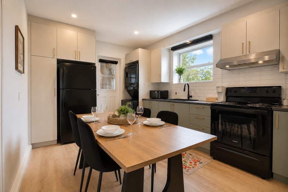 Rassemblez-vous pour les repas dans cette cuisine et ce coin repas lumineux, entièrement équipés d'appareils noirs modernes, d'armoires couleur sauge et d'une grande table à manger.