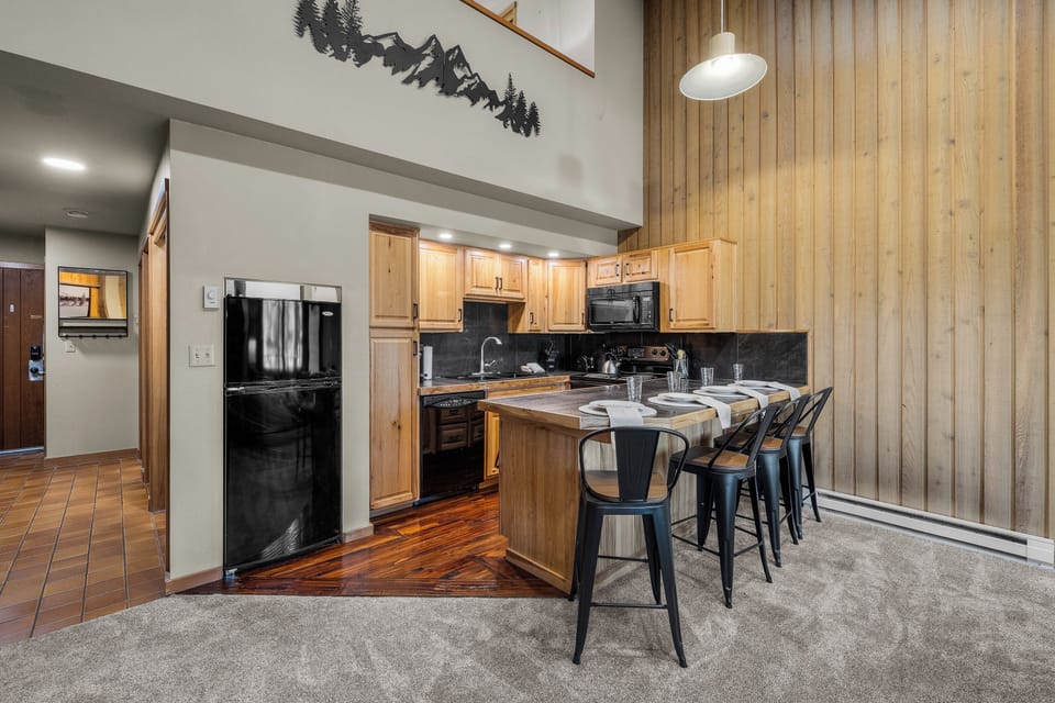 Your open-concept kitchen features warm wood cabinetry, modern appliances, and a breakfast bar with seating—perfect for gathering and preparing meals together after a day on the mountain.