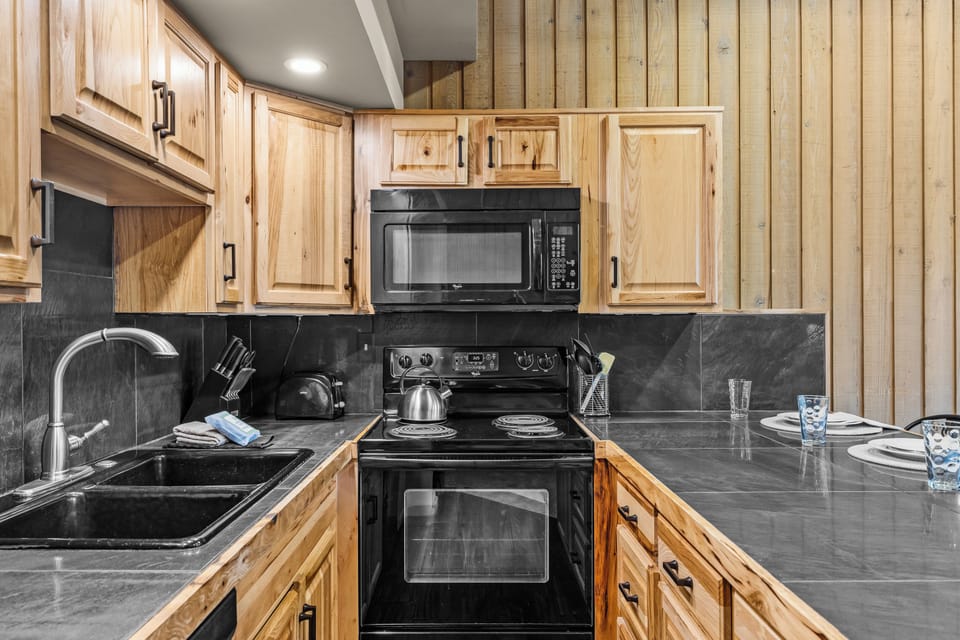 Your fully equipped kitchen features warm wood cabinetry, sleek dark countertops, and modern appliances—perfect for preparing meals together during your mountain escape.