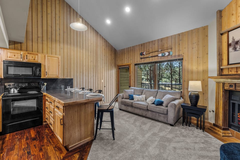 Step into your inviting open-concept retreat, where warm wood-paneled walls, a fully-equipped kitchen island, and a cozy fireplace create the perfect home base for your mountain getaway.