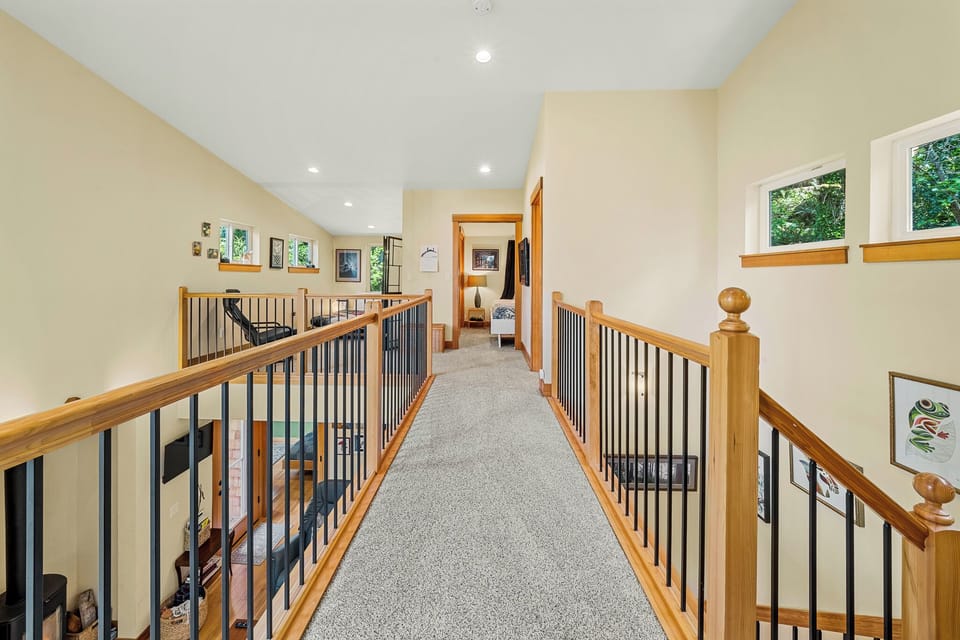Soft natural light fills this upper hallway, connecting your private bedroom spaces with thoughtful details like warm wood railings and vaulted ceilings for an open, airy retreat.