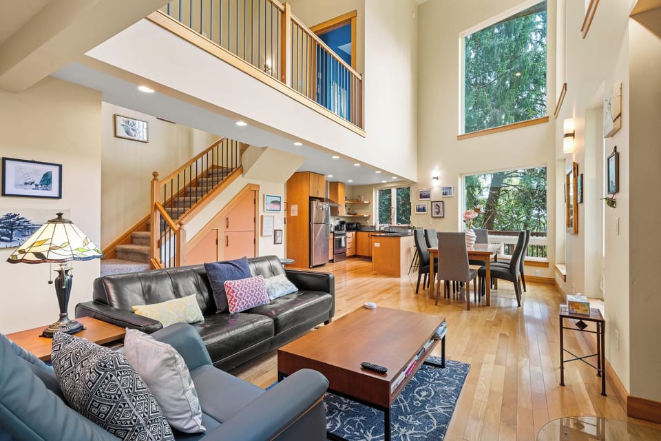 Relax in your spacious living area where soaring ceilings and sunlight through tall windows create an airy, welcoming retreat. The open layout connects seamlessly to a well-equipped kitchen and dining space.