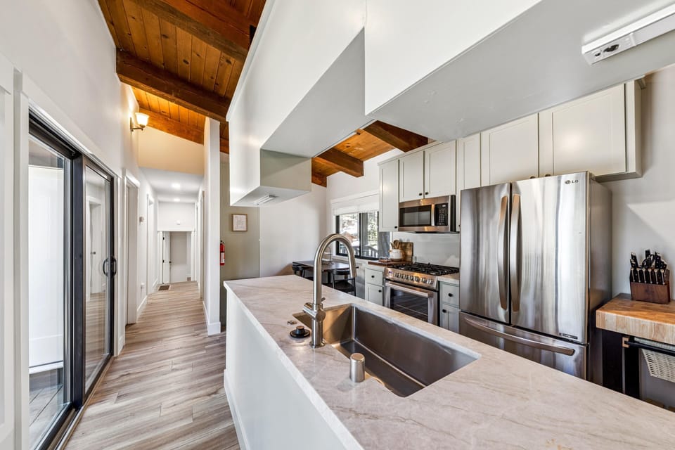 Marble countertop island with stainless steel sink overlooks stainless appliances and white cabinetry.