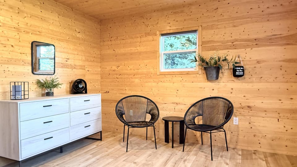 Sitting area with black woven chairs, round wooden table, and light wood-paneled walls and flooring.