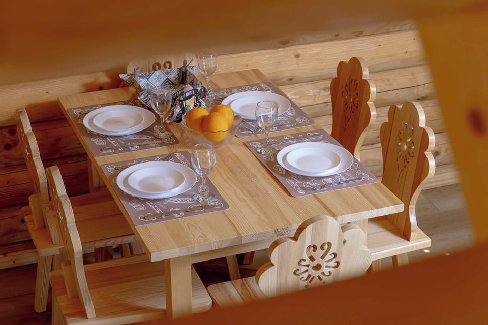 A close-up of the dining table set for a meal with a white tableware set for six people. The decorative details on the chairs reference traditional regional design.