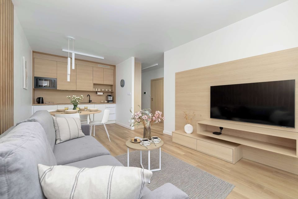 Open-concept living featuring light wood panels, a sofa, and kitchen cabinets. Modern design elements flow throughout the apartment.