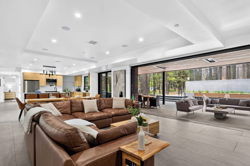 Expansive indoor-outdoor living space with a chef’s kitchen, oversized sectional, and covered lounge just beyond the glass wall.