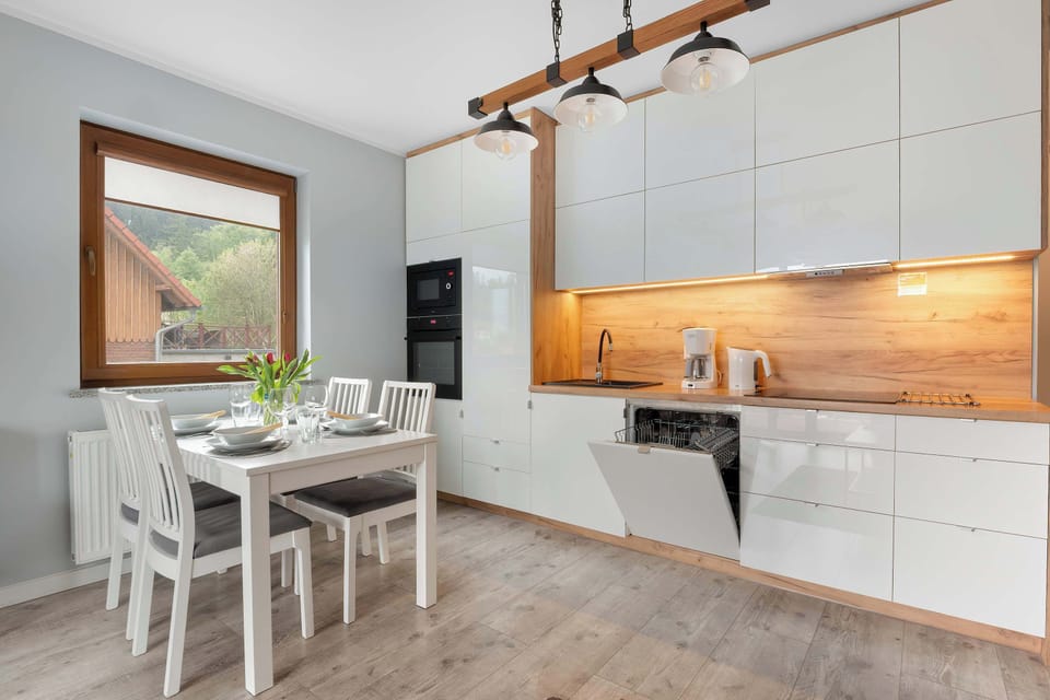 The kitchen workspace is highly functional, equipped with a built-in oven and a dishwasher integrated into the white cabinetry. Wooden backsplashes and countertops provide a warm, organic texture to the room.