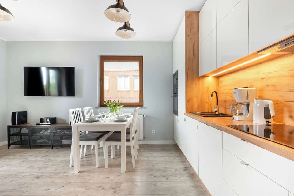 This perspective of the living area showcases the contrast between the white furniture and the dark media console under the TV. The kitchen area is visible in the background, featuring integrated appliances and under-cabinet lighting.