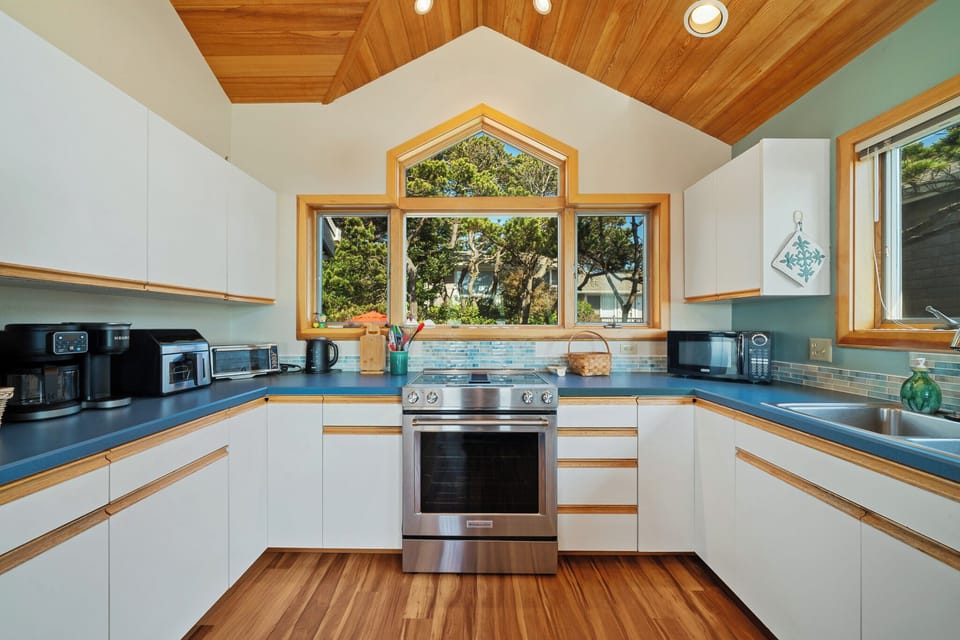 Step into this bright, inviting kitchen where your culinary creativity can flourish beneath soaring wood ceilings and abundant natural light streaming through stunning arched windows.