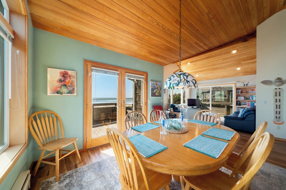 Gather around this inviting dining table where ocean breezes and warm wood surround you. Natural light pours through doors opening to your private deck, while the kitchen and cozy living space await nearby.