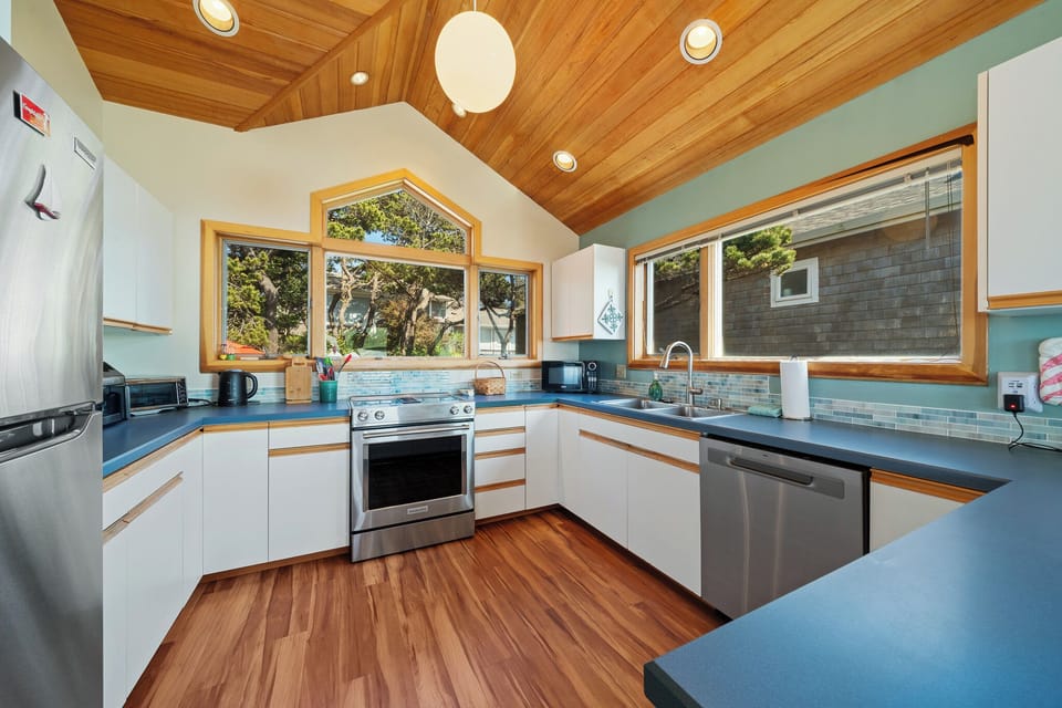 Your spacious, fully equipped kitchen features modern stainless appliances, stunning wood ceilings, abundant natural light, and inspiring garden views through the arched windows.