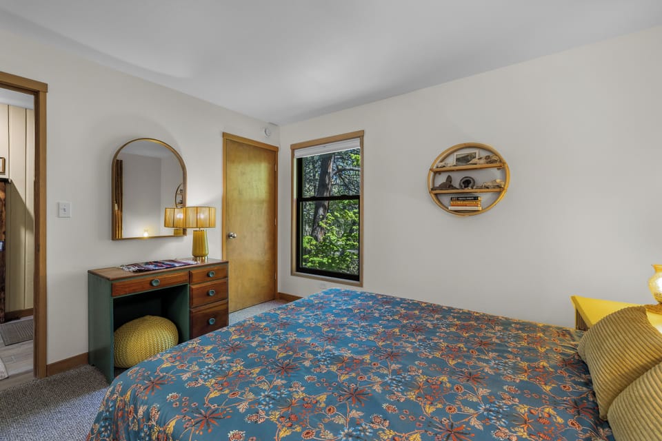 Unwind in your cozy bedroom with a plush floral duvet, vintage-inspired furnishings, and a window framing lush greenery—your personal retreat awaits.