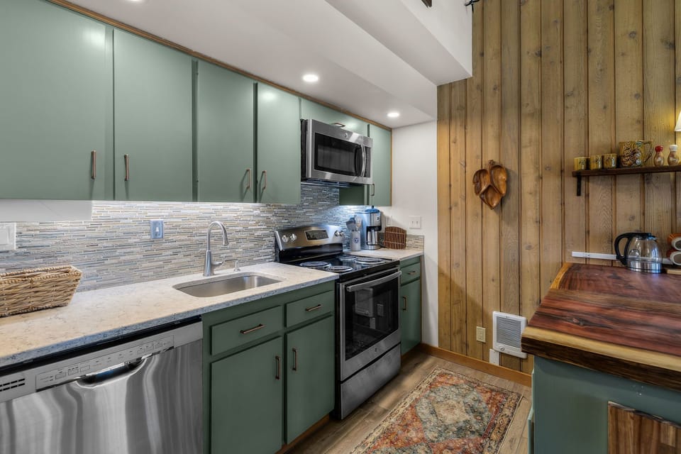 A fully equipped kitchen features modern appliances, stylish green cabinetry, and a cozy breakfast nook where you'll enjoy your morning coffee surrounded by warm wood accents.