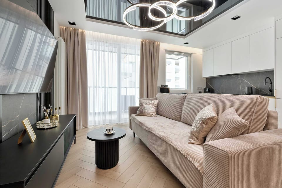 This living area view highlights the open-plan layout leading toward the balcony. Neutral tones dominate the furniture, while a large flat-screen TV sits on a sleek black cabinet.