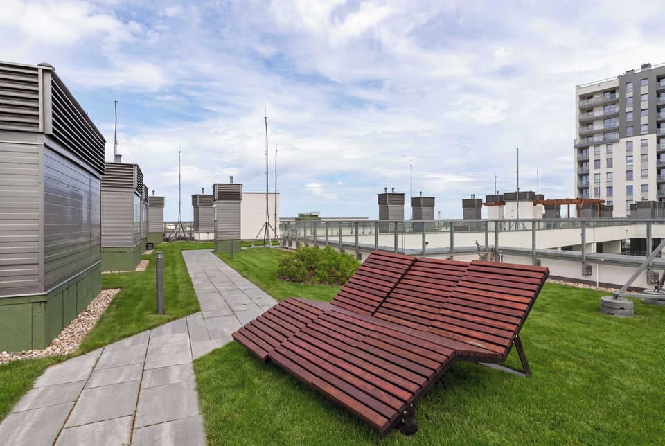 A rooftop terrace features green artificial grass and wooden lounge chairs for sunbathing. The elevated space provides a quiet outdoor retreat within the city.