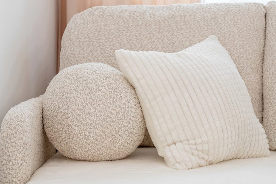 Textured throw pillows, including one round and one rectangular, rest on the soft fabric of the sofa. These details emphasize the cozy and inviting nature of the living space.