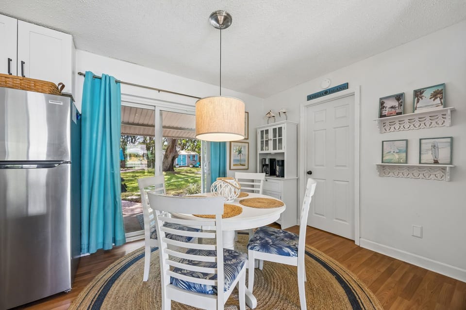 This bright dining area features coastal charm with its white table, tropical accents, and garden views through glass doors, creating your perfect spot for morning coffee or meals together.