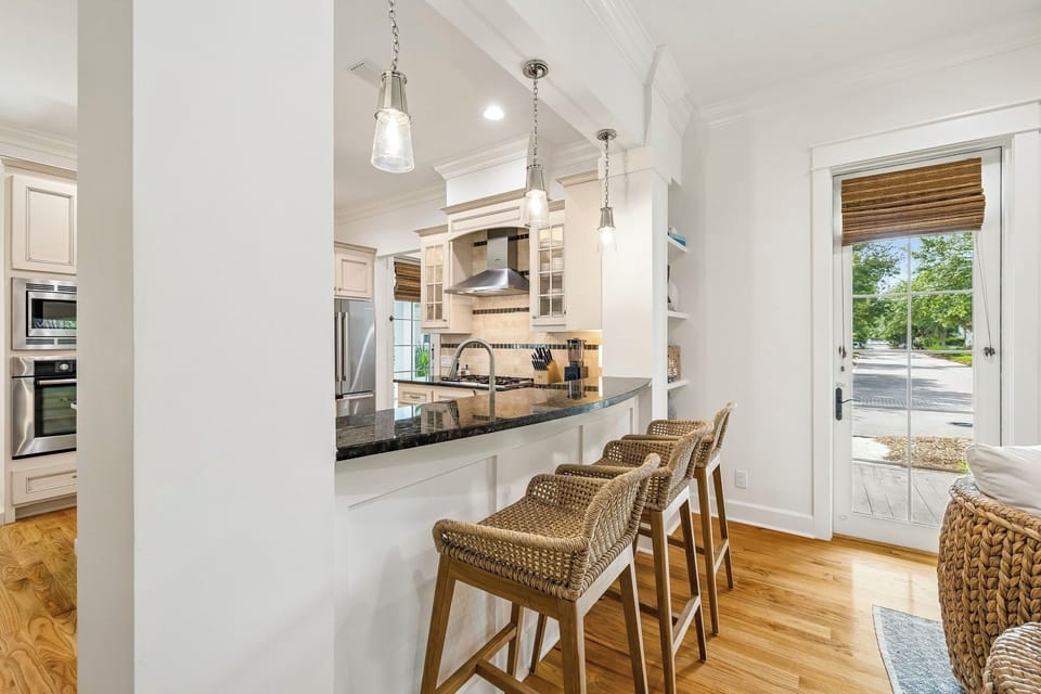 Gather around the breakfast bar in your bright, airy kitchen where white cabinetry, modern pendant lights, and polished countertops create the perfect space for morning coffee or casual meals together.