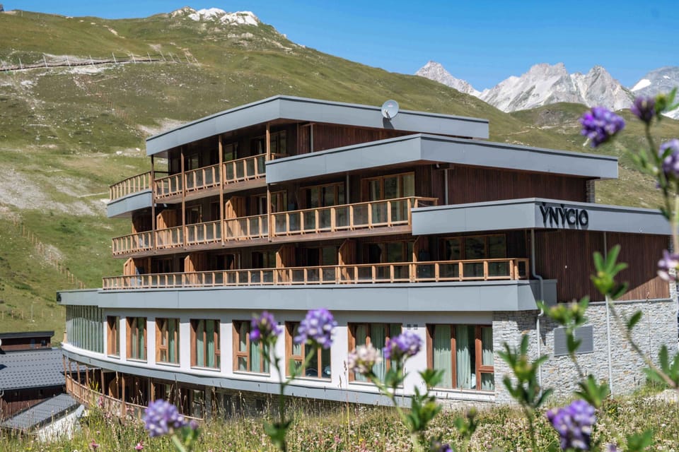 Wood-clad façade with full-width balconies running across each floor, set against the alpine slopes of Tignes Val Claret