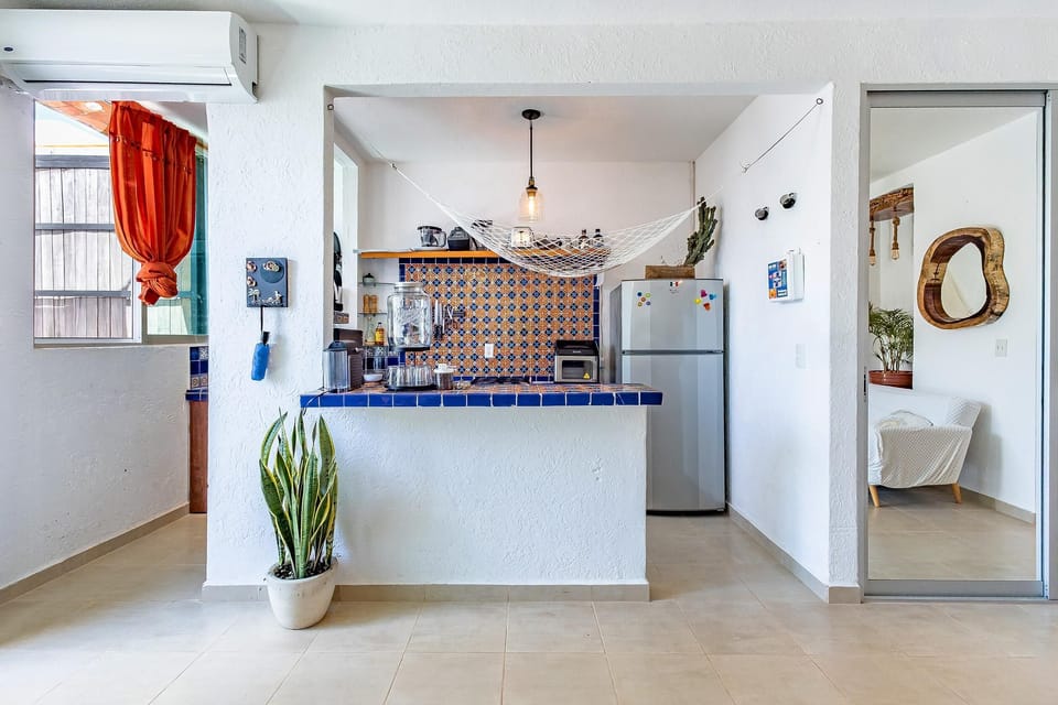 Blue-tiled kitchen bar with patterned backsplash,  fridge, hanging net for fresh , and potted snake plant.