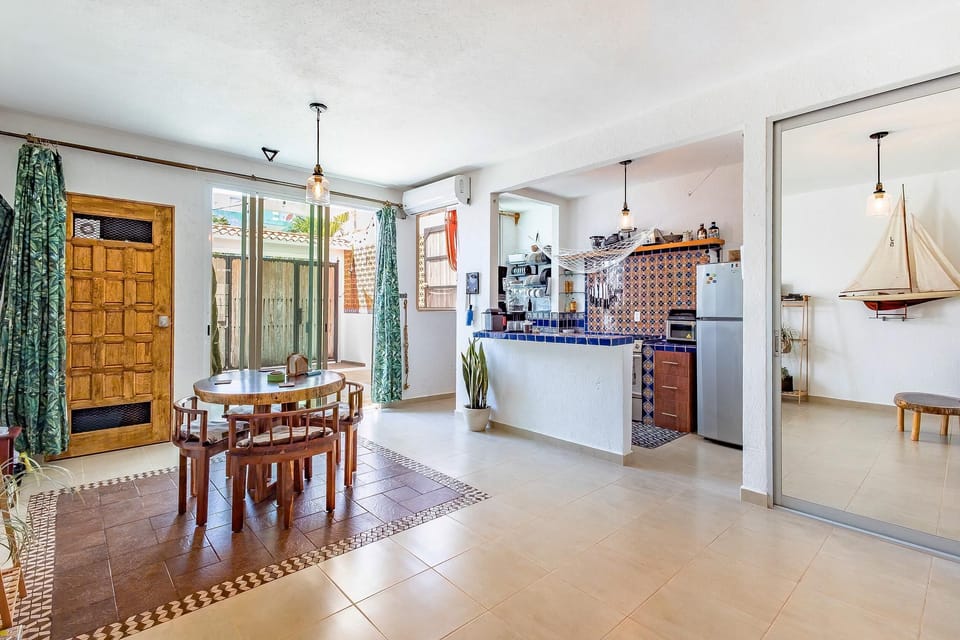 Dining area with round wooden table and stools, adjacent to tiled kitchen bar with patterned blue backsplash.