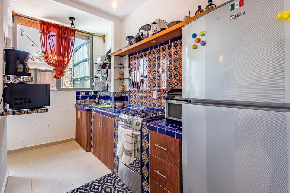 Kitchen with blue patterned tile backsplash, appliances, and wooden cabinetry.