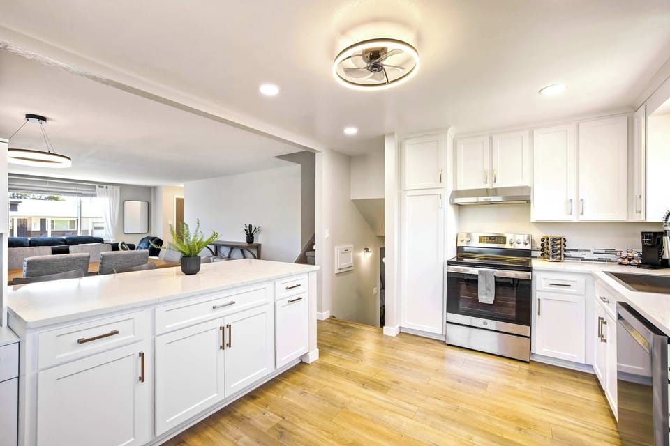 The kitchen runs long and bright with white shaker cabinets, stainless appliances, and warm wood floors that carry through from the main level. A flush ceiling light and recessed lighting keep the workspace well lit from every angle.
