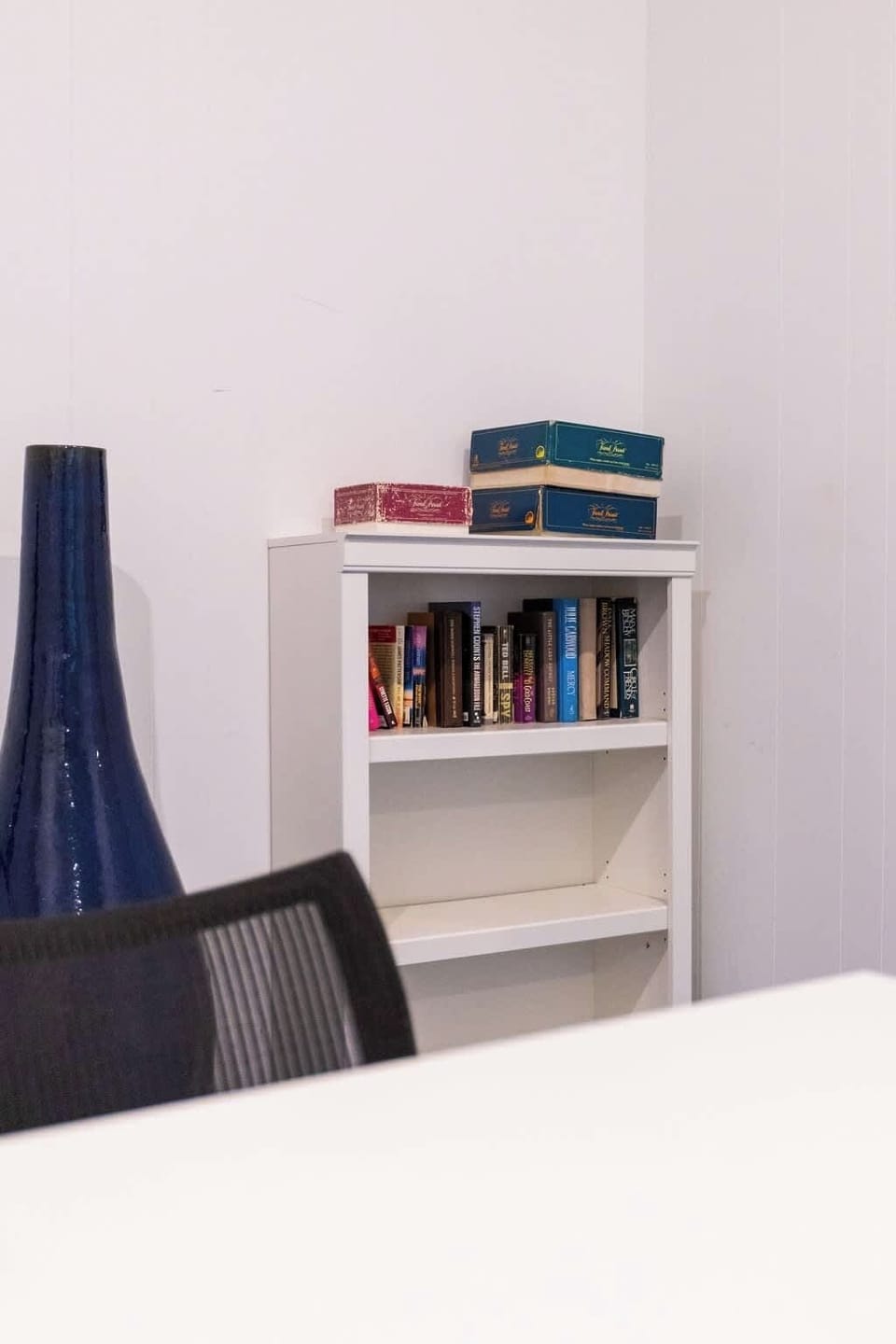 White bookshelf filled with colorful novels and paperbacks in a shared library area, offering guests a cozy reading corner.
