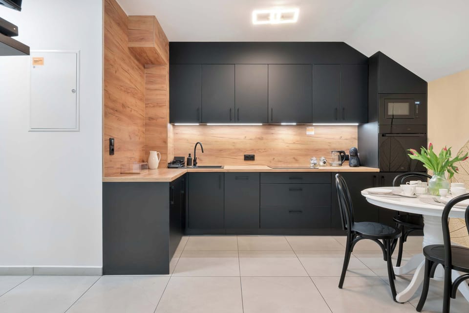 A stylish kitchen with black cabinetry, wooden finishes, and a dining table nearby.