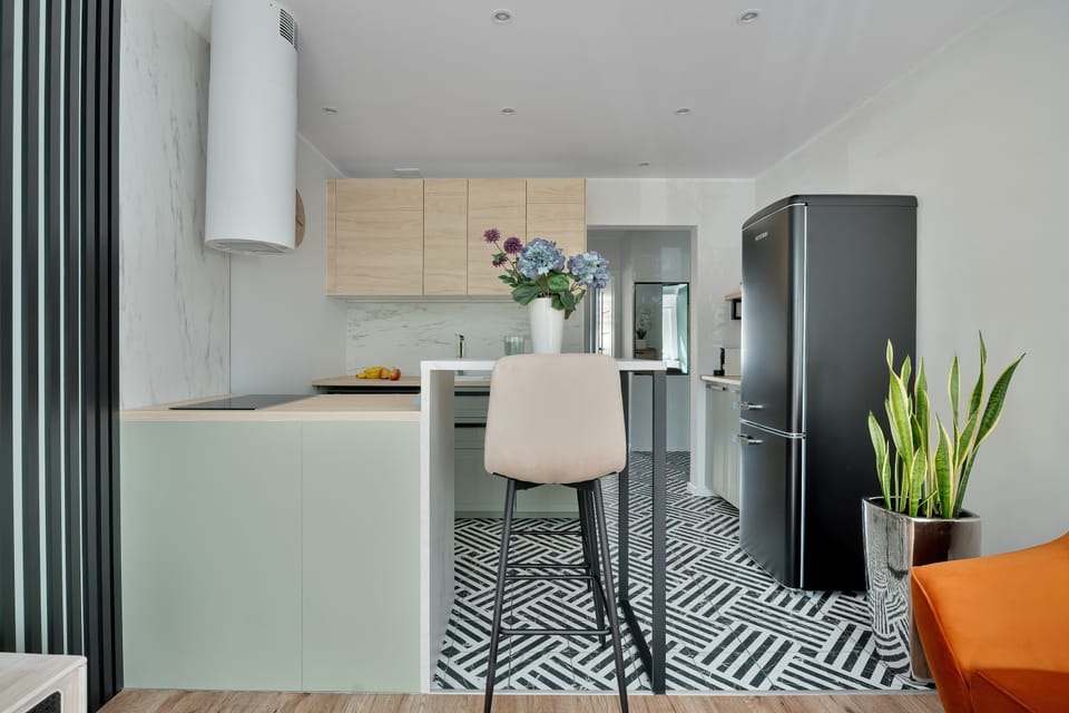 The kitchen area features a modern breakfast bar with a high stool and a sleek black refrigerator in the background.