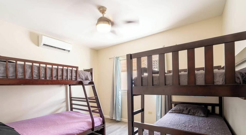 Spacious third bedroom features a queen bed, wood accents throughout, large windows, distressed wooden furniture, and beach-inspired decor .