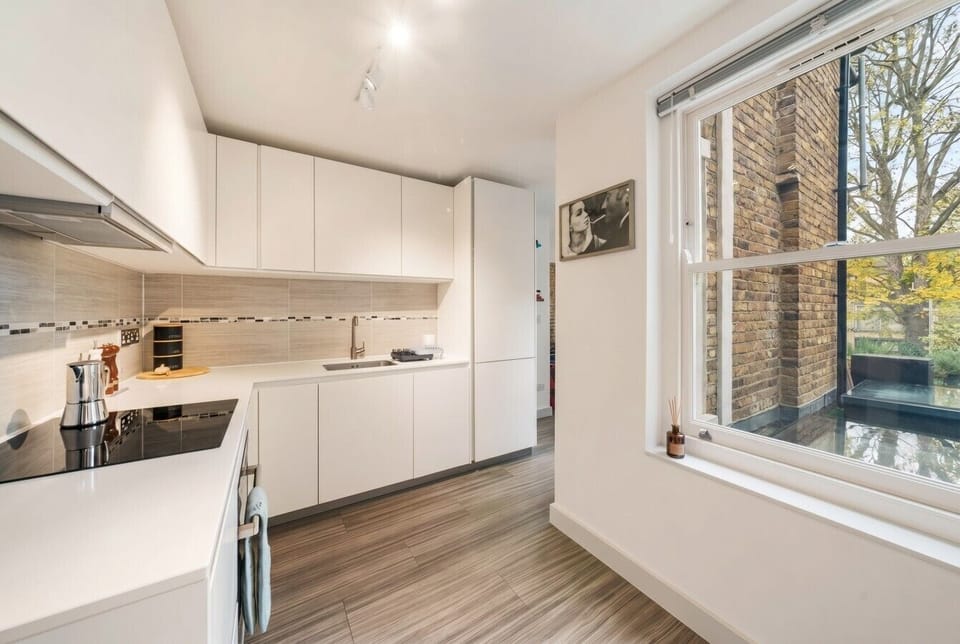 Sleek white kitchen with induction hob and a pretty window overlooking the terrace.