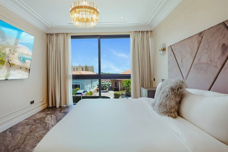 Modern bedroom setting showing a textured dust-rose headboard paneling beside a large window with neighborhood views.