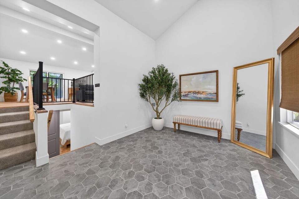 Grand entryway featuring soaring vaulted ceilings, custom hexagon stone tile floors, and a sun-filled foyer with seating bench and gold-framed full-length mirror. Open sightlines to the main living level create a stunning first impression.