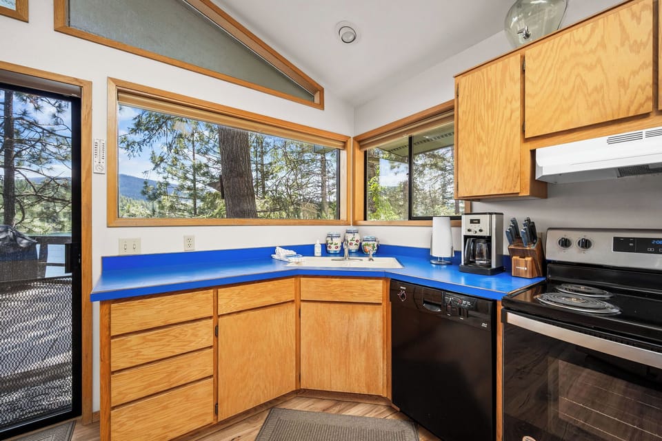 Cook with a view through expansive windows framing towering pines and distant mountains. Your kitchen flows seamlessly onto the deck, perfect for morning coffee or evening meals in nature's embrace.