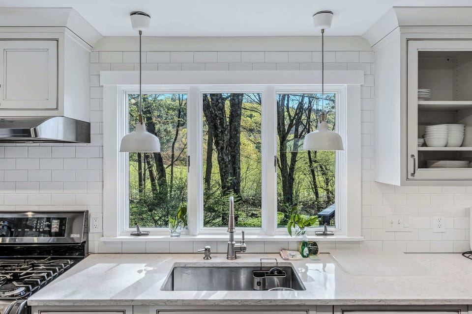 Kitchen sink with pendant lighting and a peaceful woodland view through the window