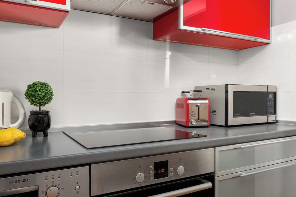 Modern kitchenette with red cabinets, built-in oven, microwave, and dining area.