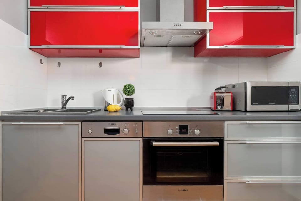Modern kitchenette with red cabinets, built-in oven, microwave, and dining area.