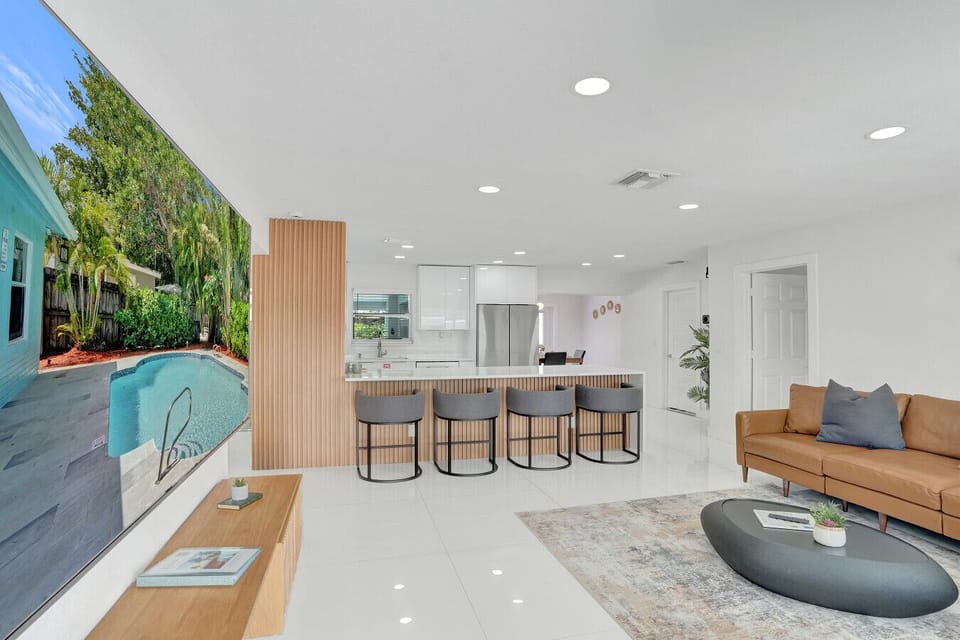 Cinema-style 100-inch TV with rich subwoofer audio in a bright living room flowing into a modern kitchen island