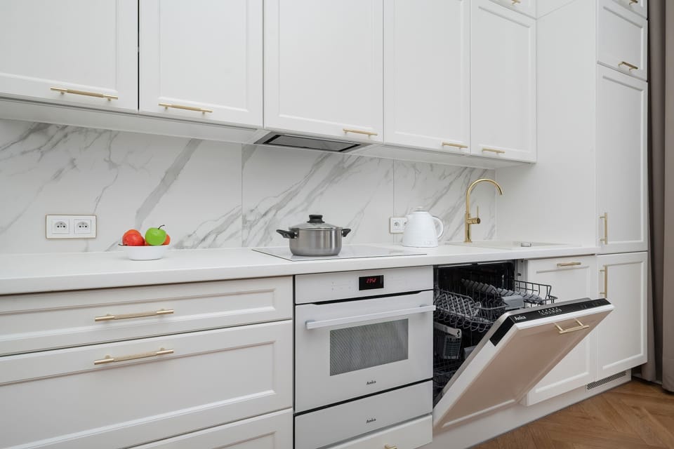 A white kitchen with clean cabinetry, marble accents, and a partially open dishwasher.